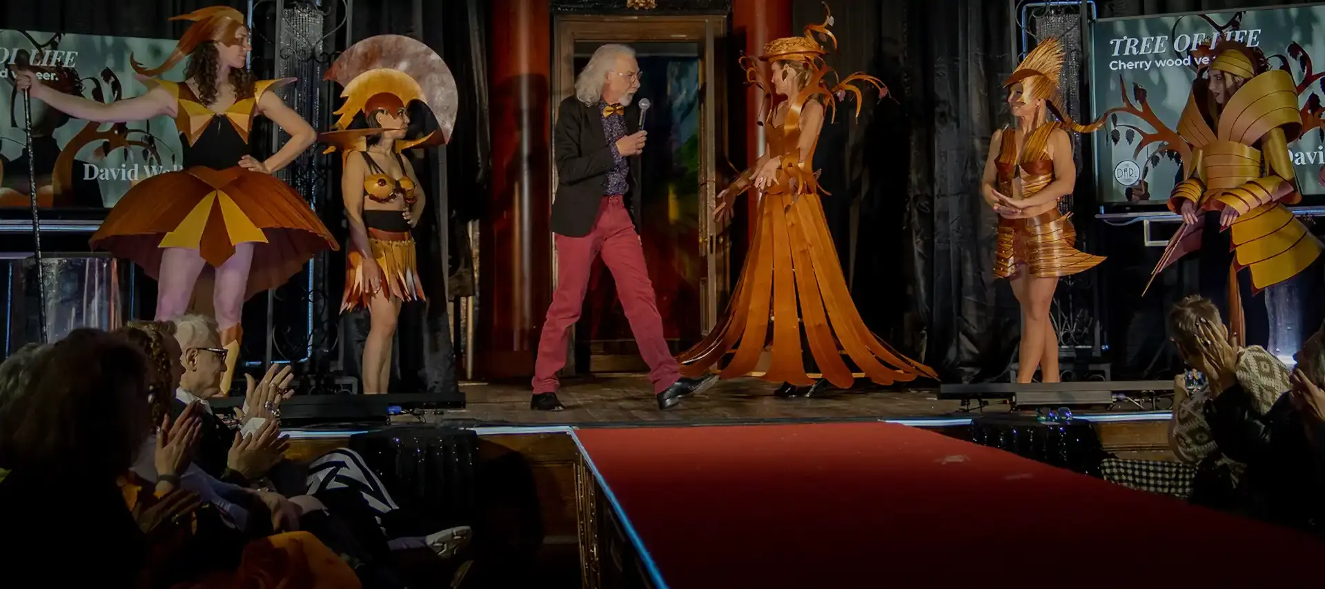 Artist David Walker on stage with several models wearing unique dresses fashoined from wood